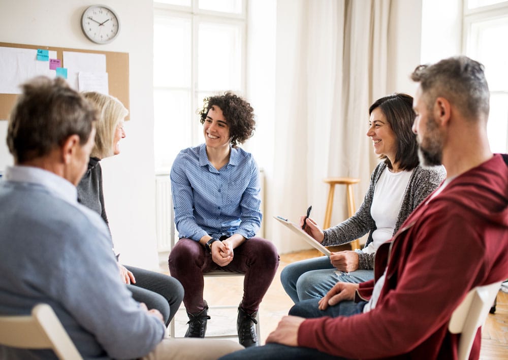 A group of middle-aged adults sitting in a circle and laughing with one another during a group counseling session