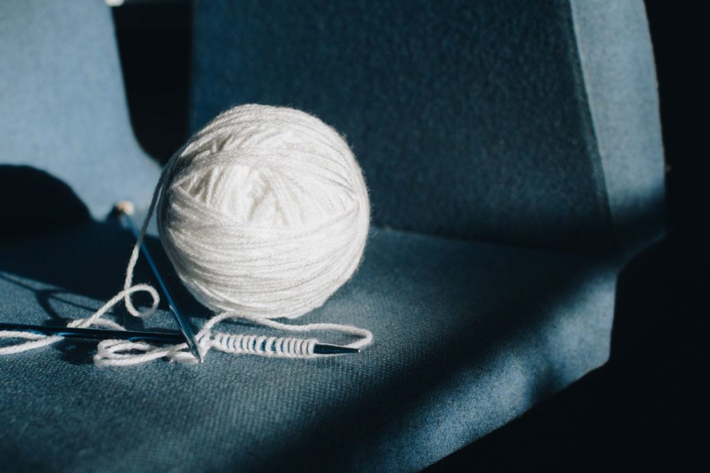 A ball of white yarn and two knitting needles on a blue chair