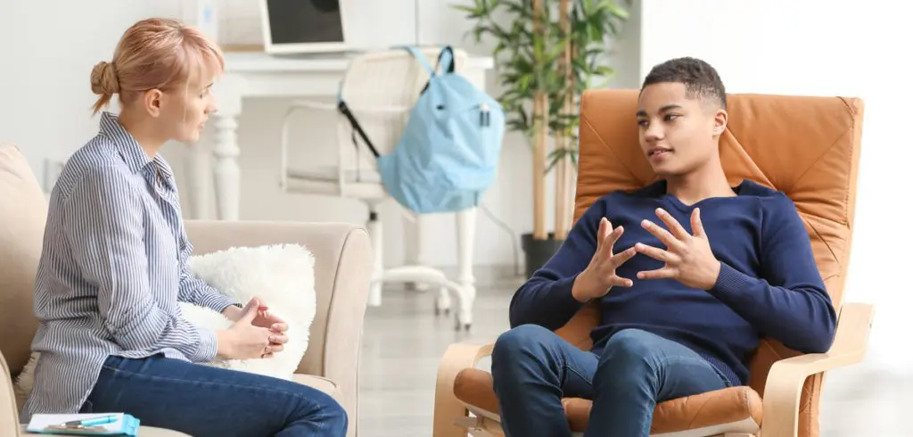 Teenage boy in an armchair talking with his therapist in a daylight-filled room