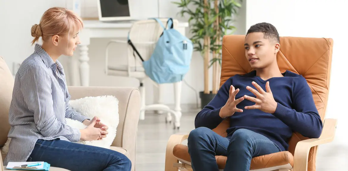 Teenage boy in an armchair talking with his therapist in a daylight-filled room