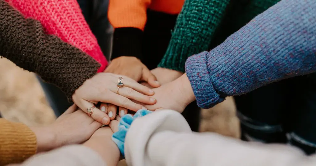 A closeup of a group of young people stacking their hands in a supportive huddle.