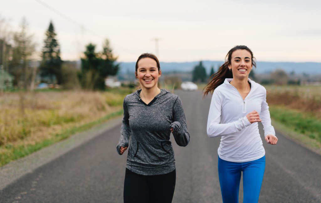 Two smiling teenage girls running together on a rural highway