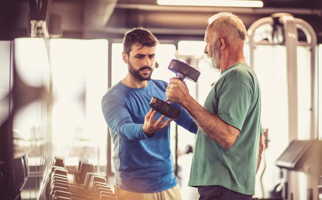 A senior man lifting weights with his personal trainer