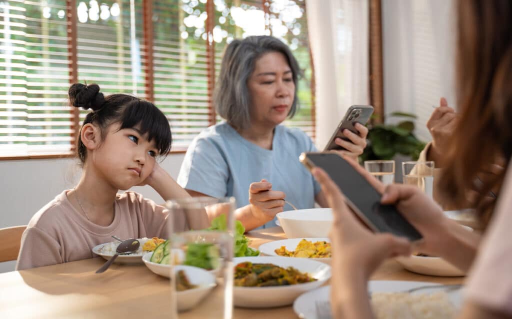 Adults using smartphones at the dinner table with a bored child