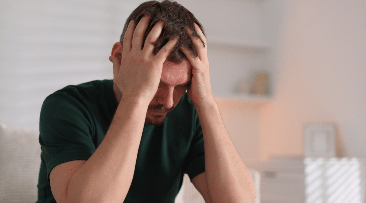 A man sitting, holding his head in his hands.